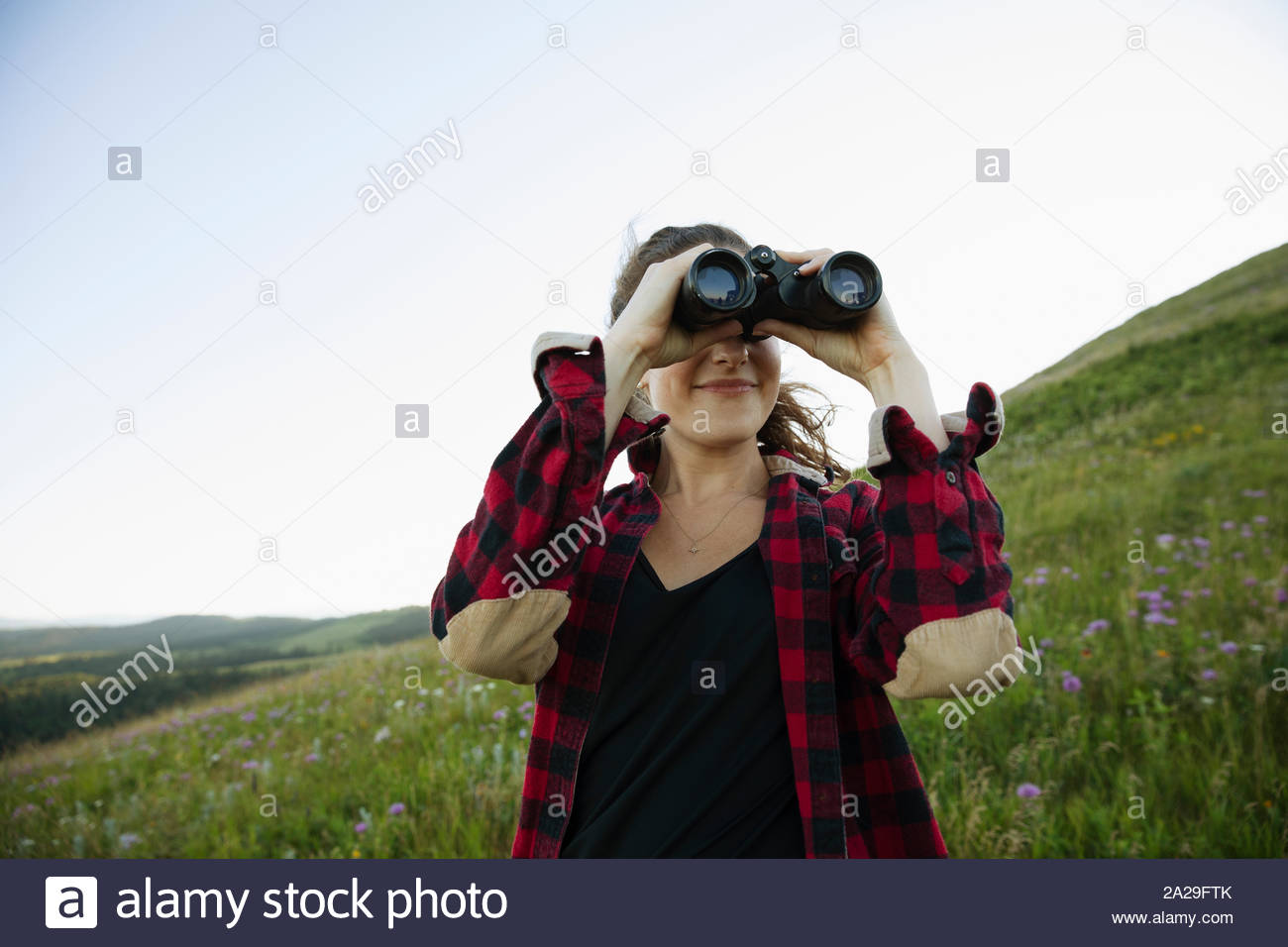 Young woman on hillside using binoculars Stock Photo