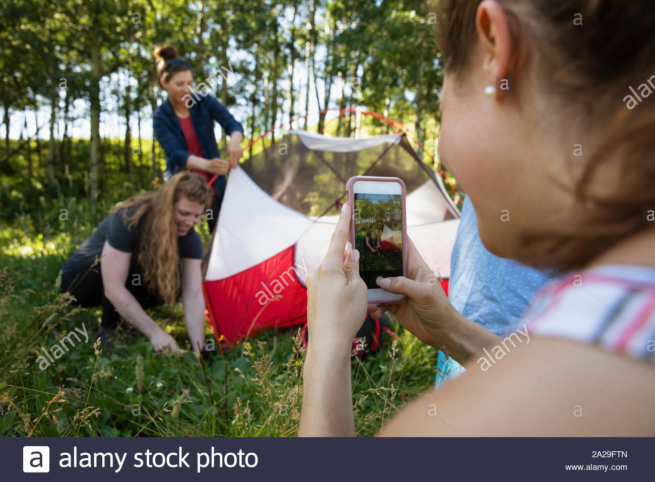 Woman filming friends putting up tent Stock Photo