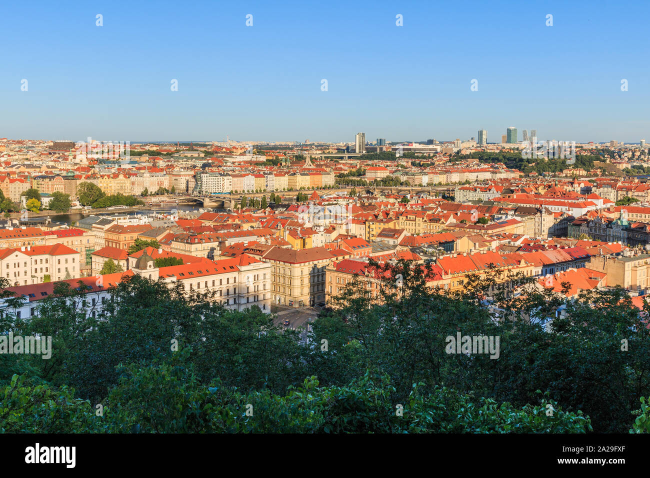 Panoramic view over the roofs and historical buildings of Prague the capital of the Czech Republic in a sunny day with trees and shrubs in foreground Stock Photo