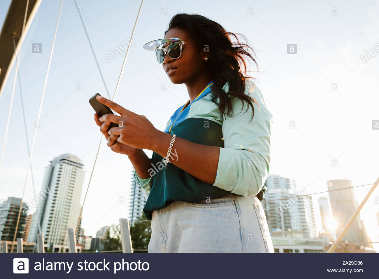 Cool young woman using smart phone in sunny city Stock Photo