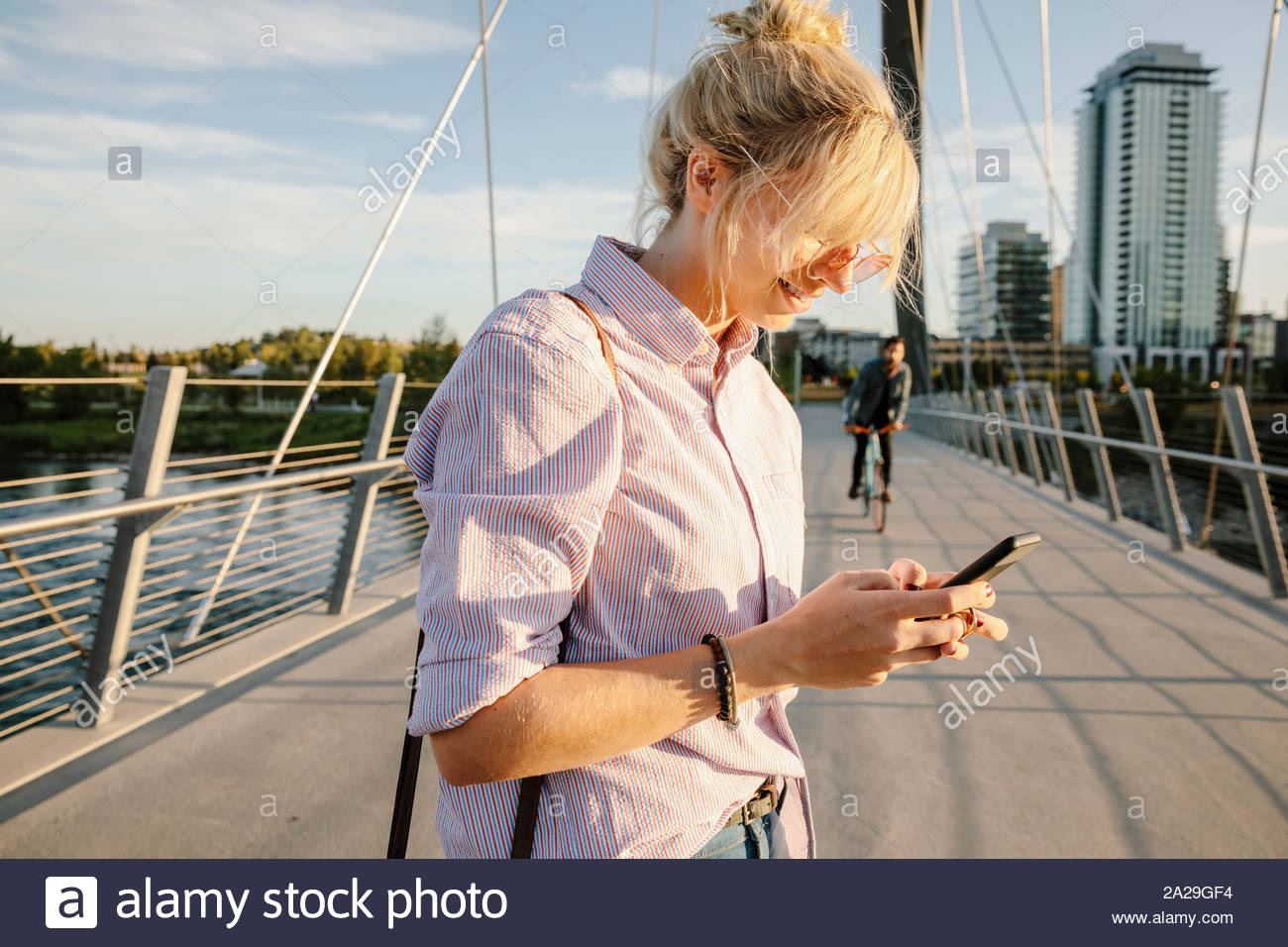 Young woman using smart phone on sunny, urban bridge Stock Photo