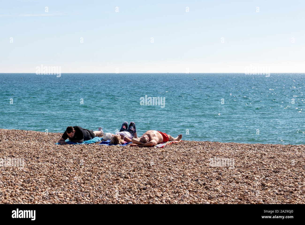 People sunbathing on a British pebble beach on a warm summers day with clear blue sky Stock Photo