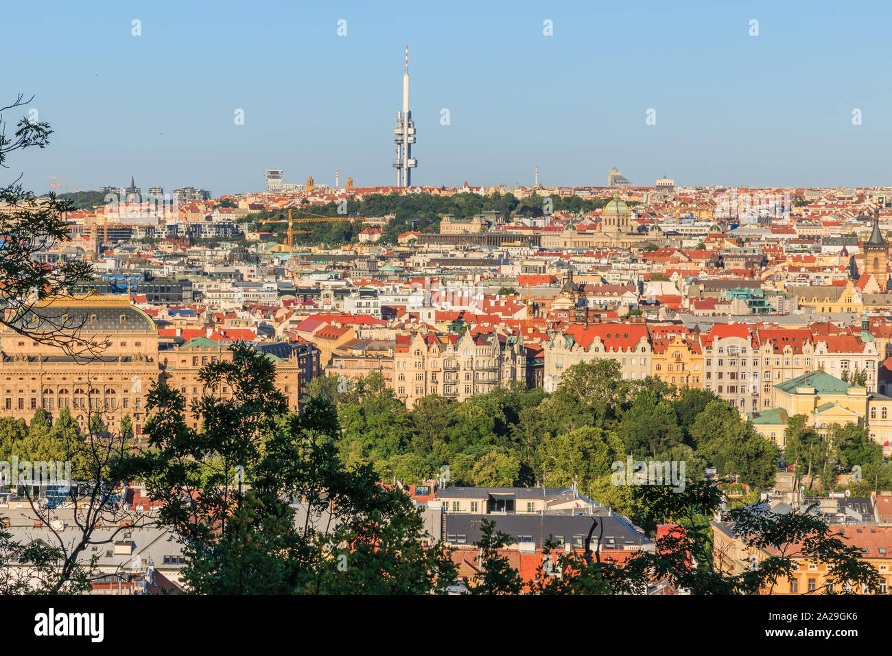 View over the rooftops and historical buildings of Prague the capital of the Czech Republic with TV tower on a sunny day with blues sky and bushes in Stock Photo