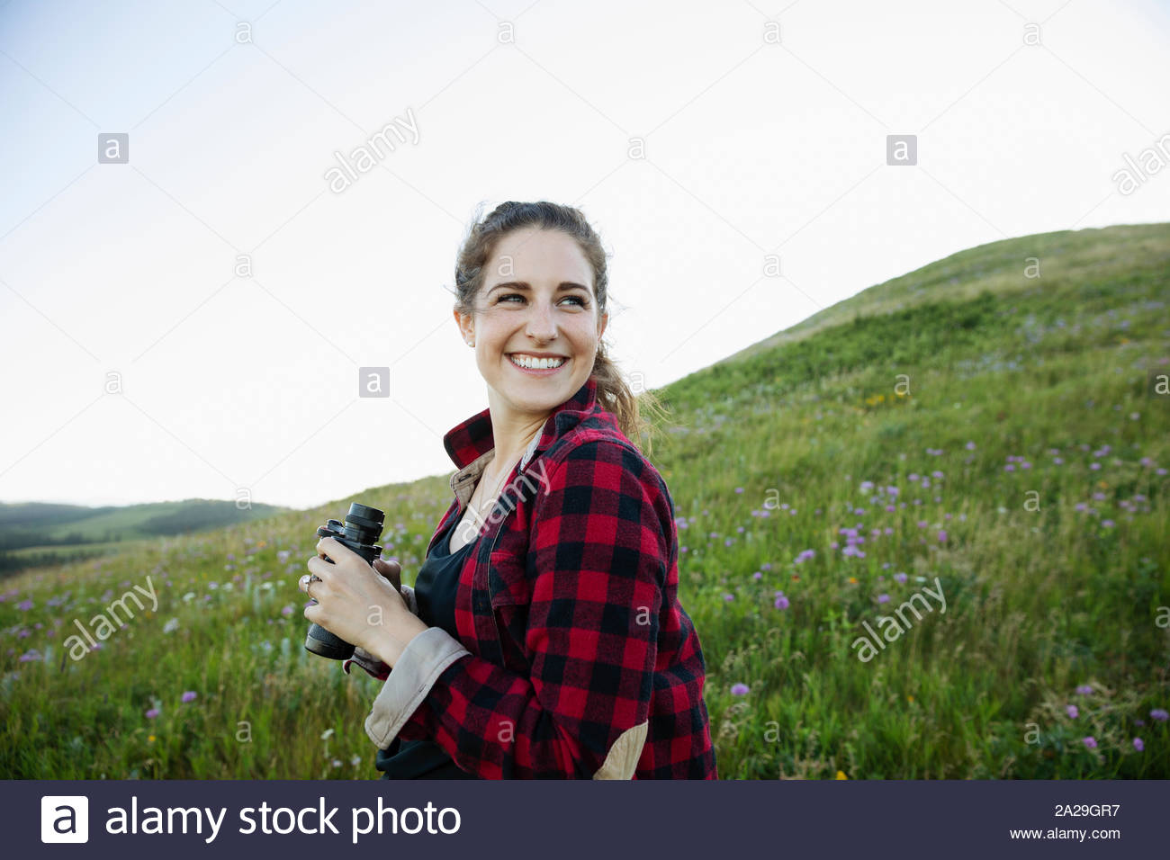Young woman on hillside with binoculars smiling Stock Photo