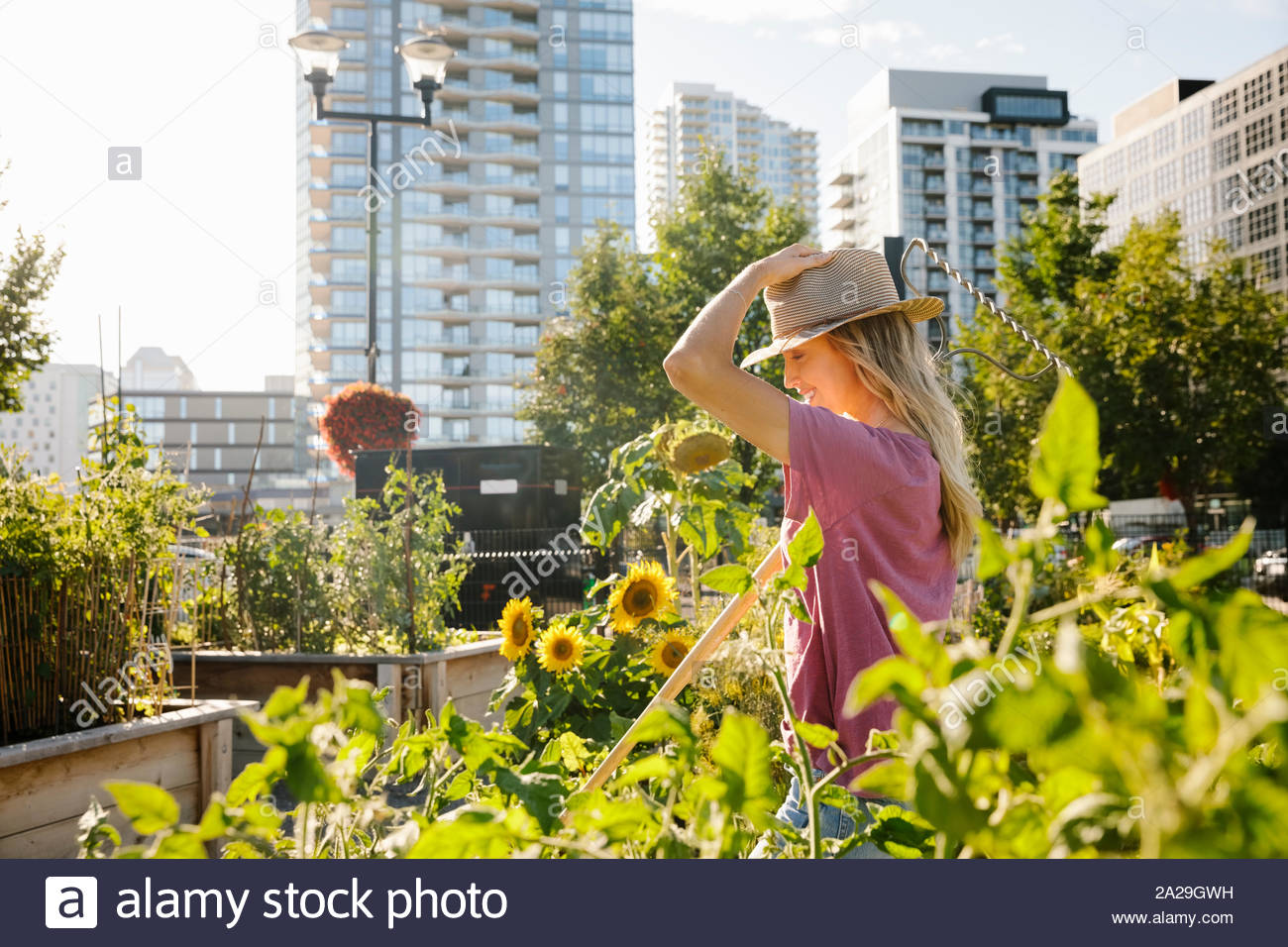 Happy young woman with sun hat in sunny, urban community garden Stock Photo
