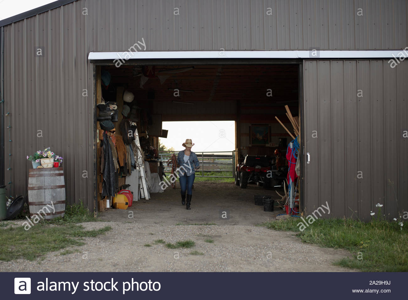 Woman walking out of barn with horse tack Stock Photo