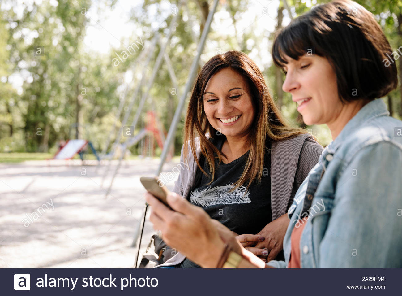 Two women in park using smartphone and smiling Stock Photo