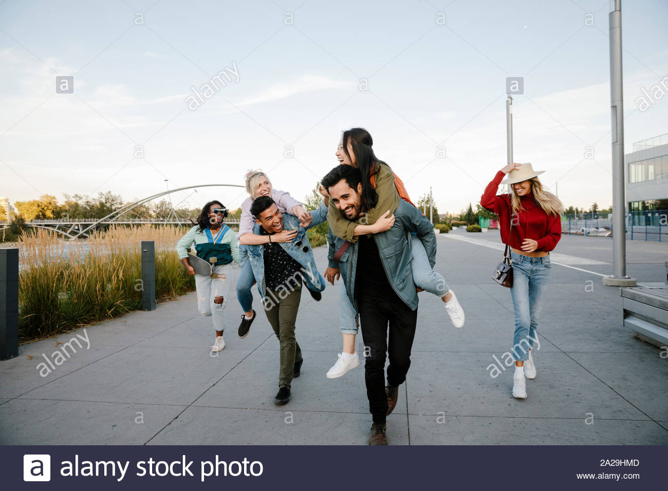 Playful young adult friends piggybacking on boardwalk Stock Photo