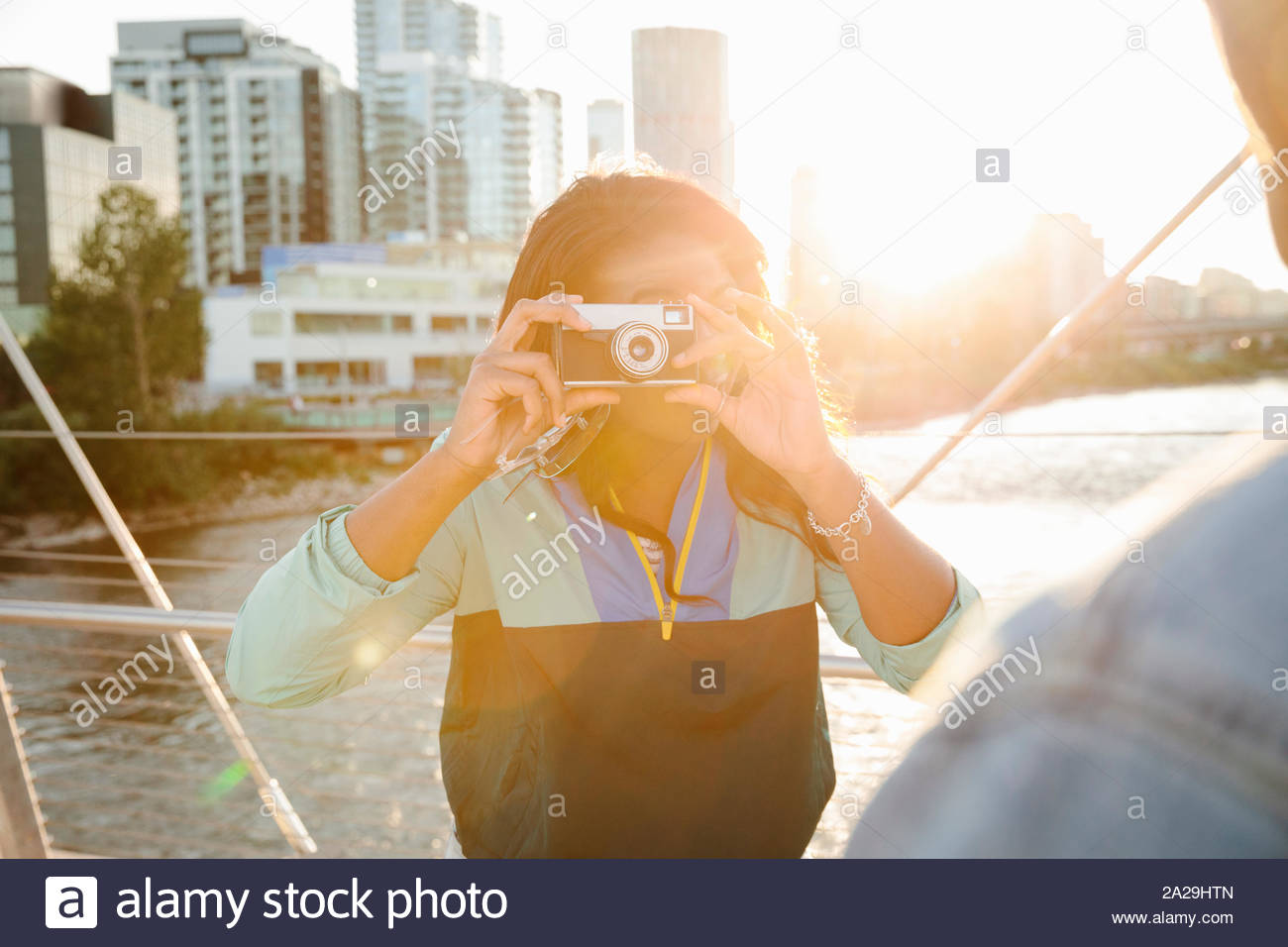 Young woman using retro camera on sunny, urban bridge Stock Photo