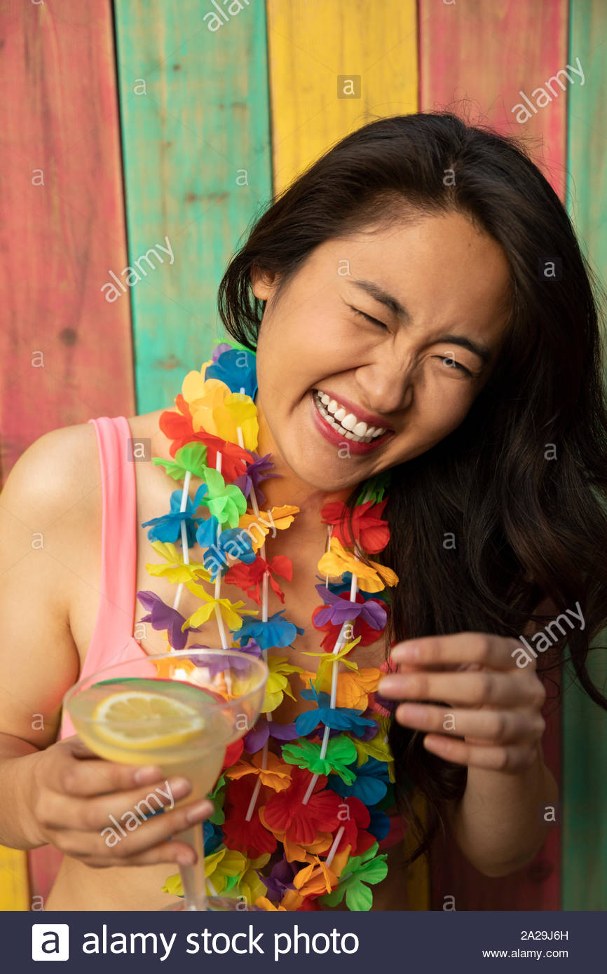 Portrait carefree, happy young woman wearing leis, laughing and drinking margarita on summer patio Stock Photo