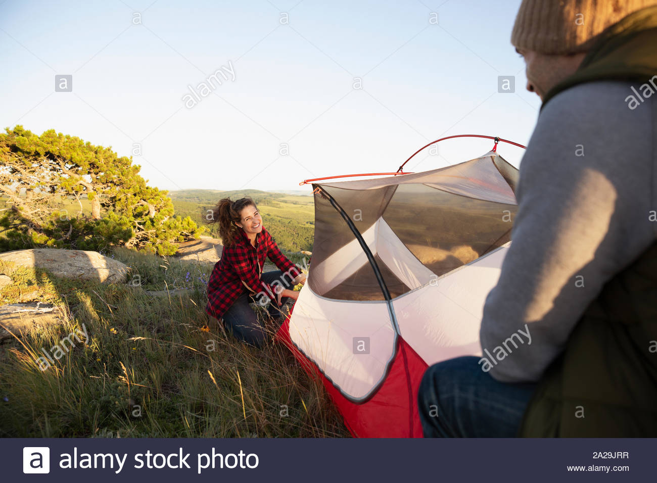 Young couple pitching tent in sunlight on hill Stock Photo