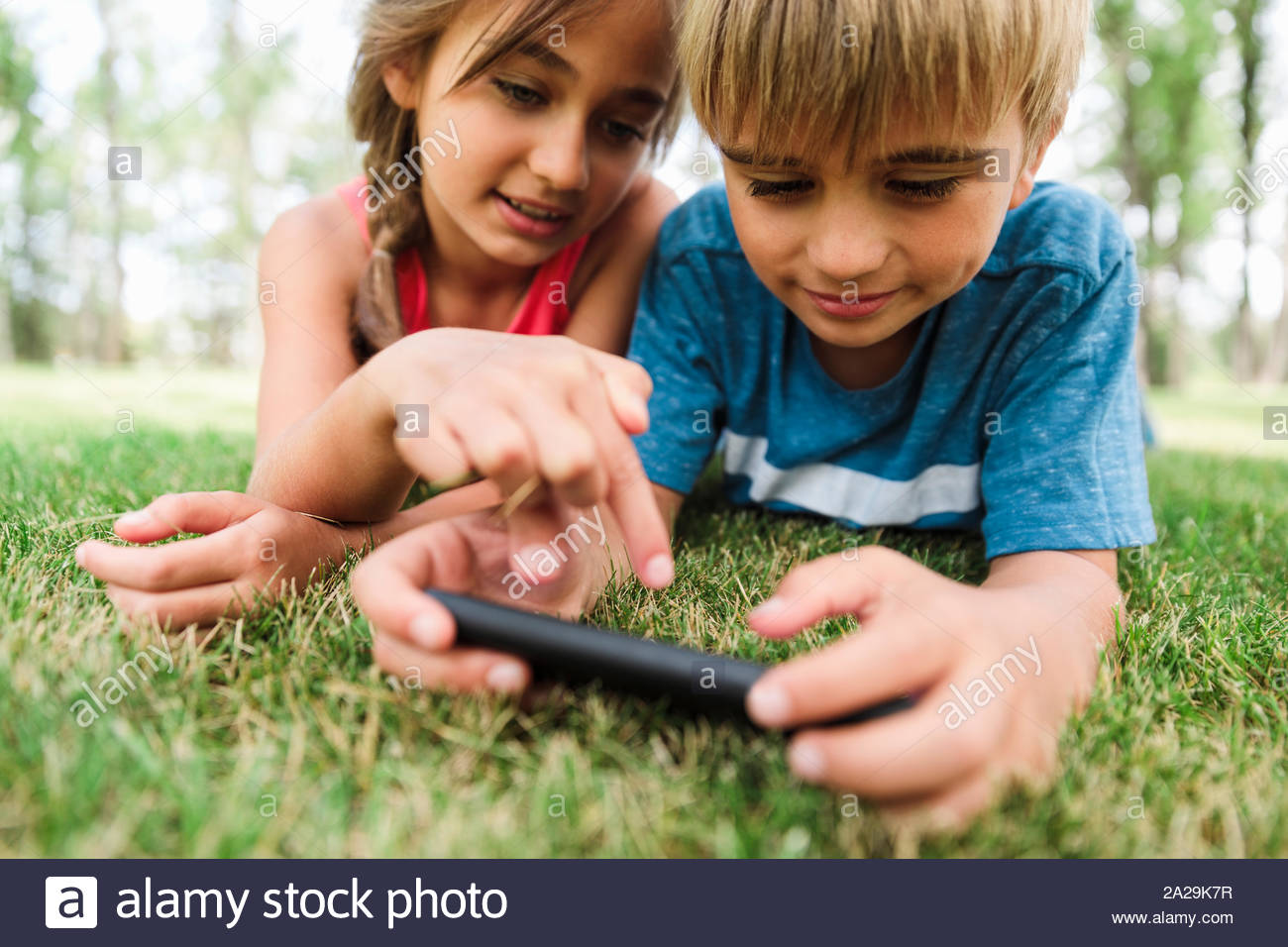 Boy and girl lying on grass using smartphone Stock Photo