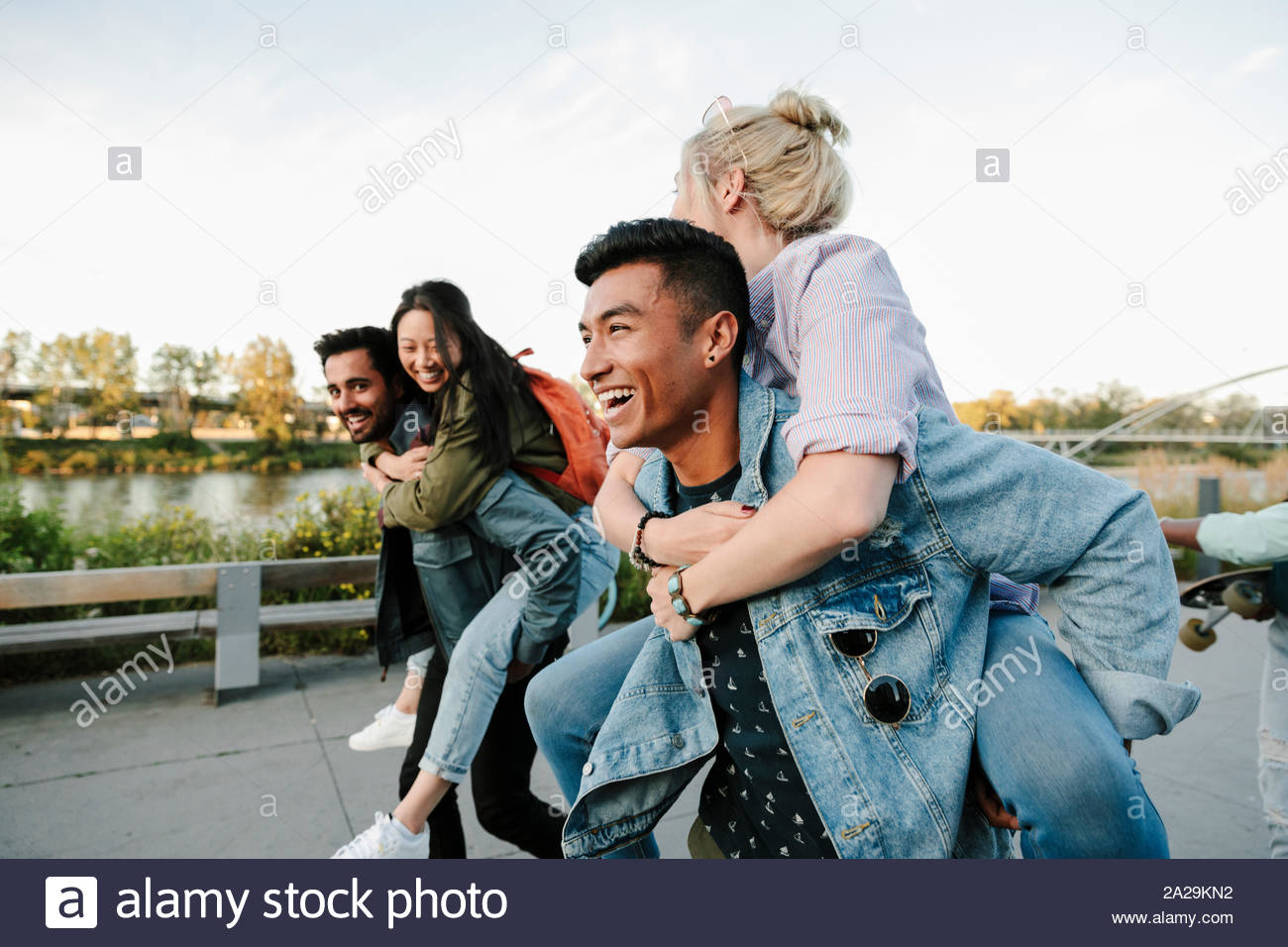 Playful young couples piggybacking along waterfront Stock Photo