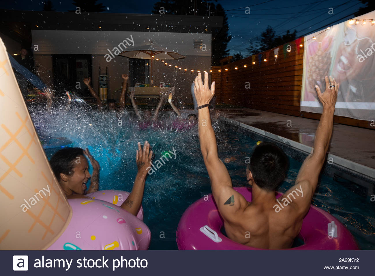 Friends cheering, splashing in summer swimming pool at night Stock Photo