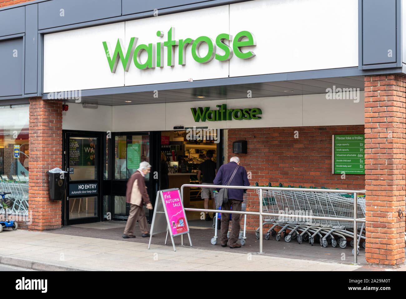 he exterior or shop front of a Waitrose supermarket with shoppers entering and a row of shopping trollies Stock Photo