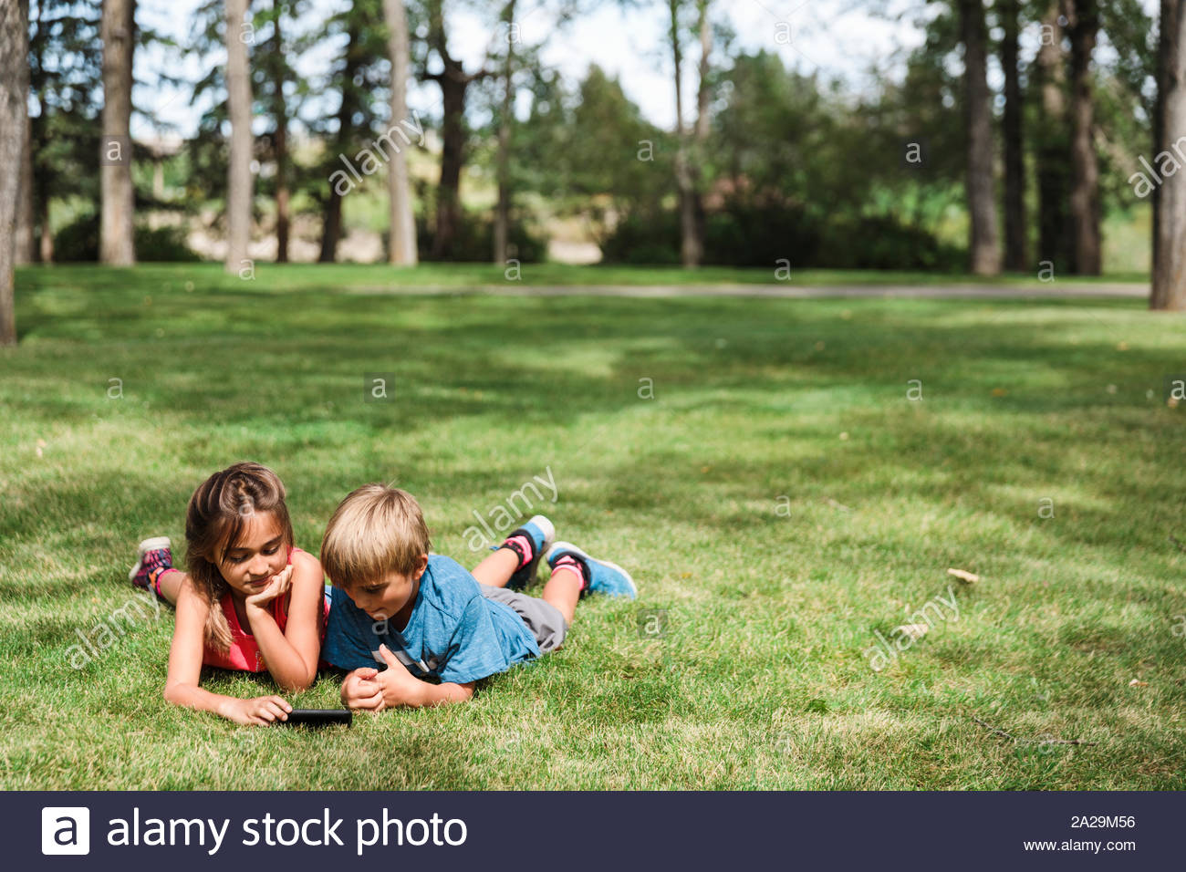 Boy and girl lying on grass using smartphone in park Stock Photo