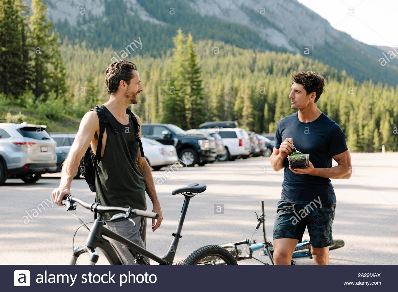 Male mountain biker friends talking and eating in parking lot Stock Photo