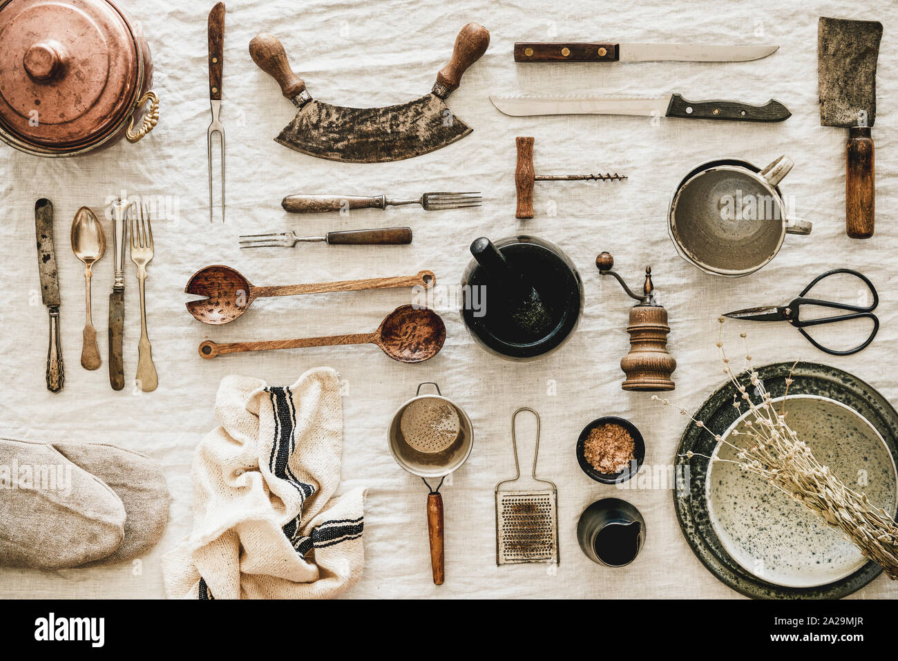 Flat-lay of various kitchen utensils, rustic tablewear, plates, dishes, glasswear, pan, scissors, corkscrew, textile for cooking over white linen tabl Stock Photo
