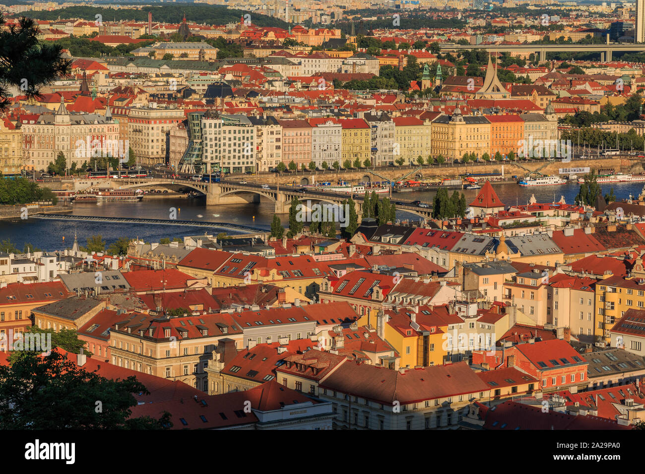 Panoramic view from viewpoint Petrin hill over the rooftops of Prague in district Mala Strana with Vltava and roads, bridge and houses on the shore in Stock Photo