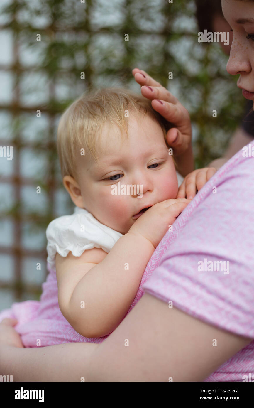 Young redhead babywearing mother carry her sleepy one year old baby