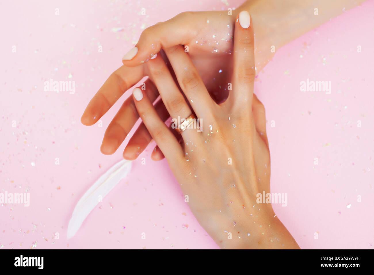 beautiful manicured woman hands with white feather on pink background, wearing wedding ring Stock Photo