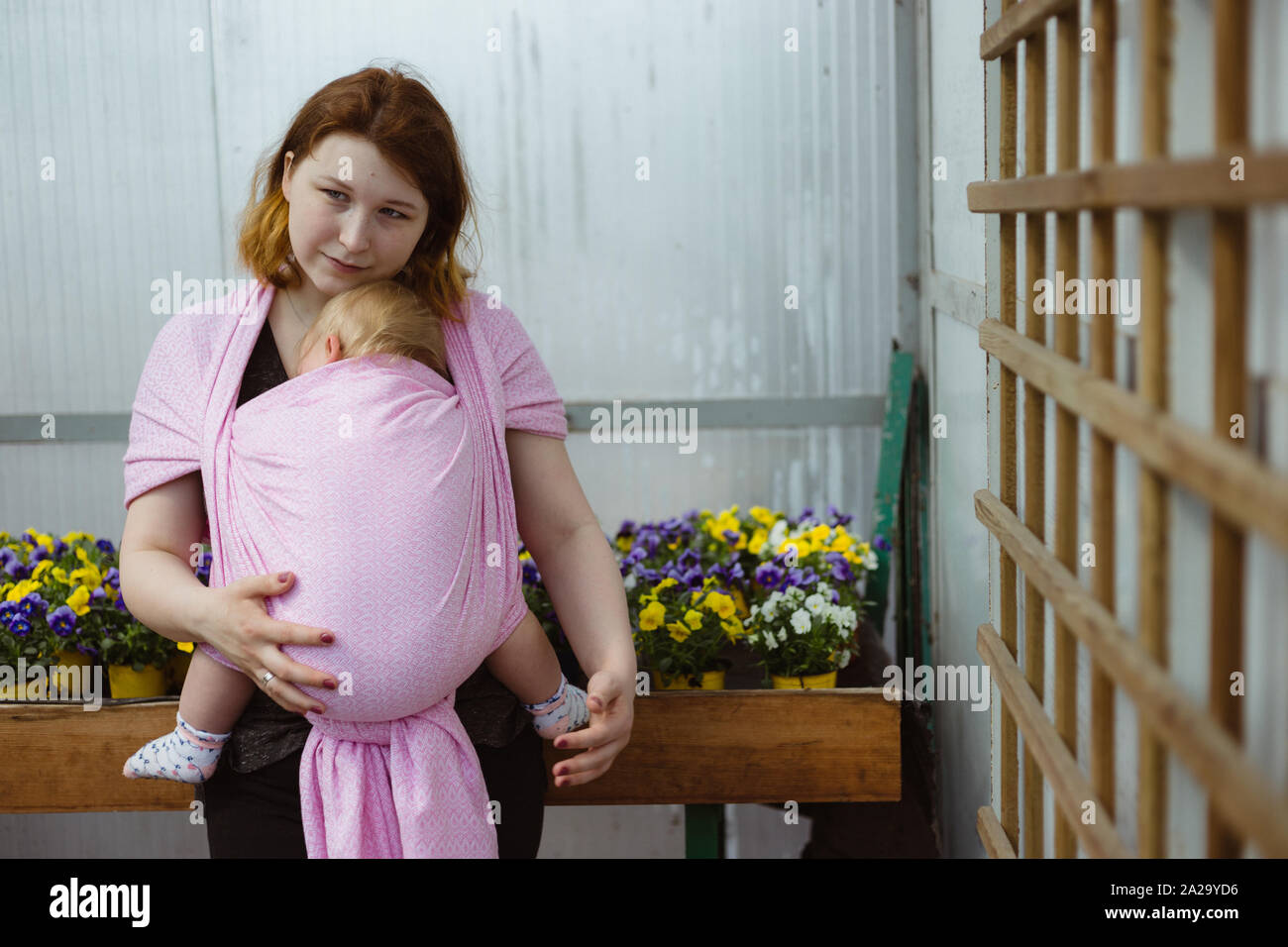 Mother carrying sleeping infant daughter in a sling wrap. Babywearing