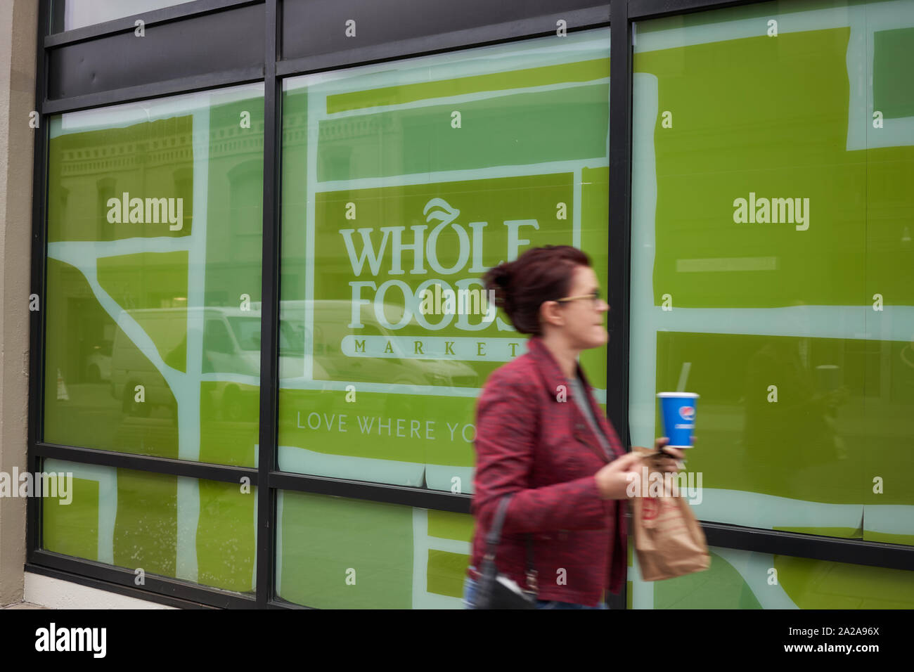 Portland, Oregon, USA - Sep 27, 2019: A woman with a to-go lunch bag and a soda outside a Whole Foods Market store in downtown Portland. Stock Photo