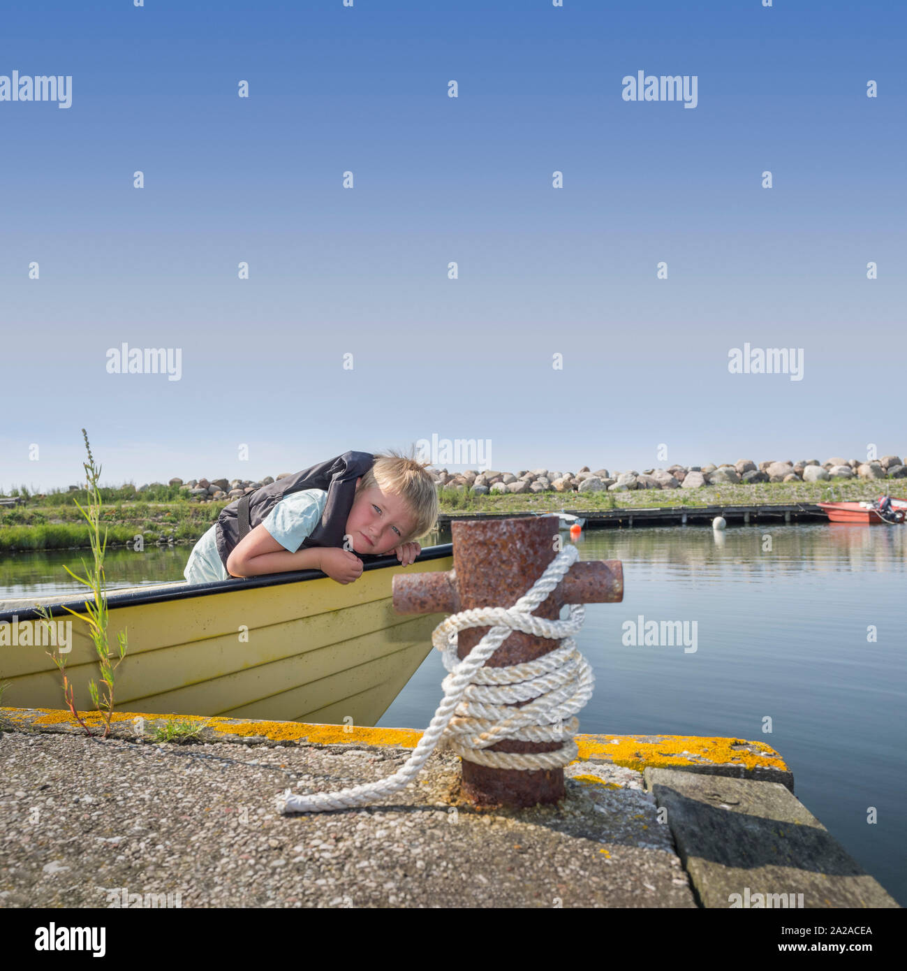 Young boy with life jacket in a moored boat at a jetty Stock Photo