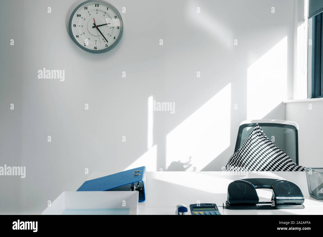 Empty office desk and chair with a clock above emphasising lateness Stock Photo