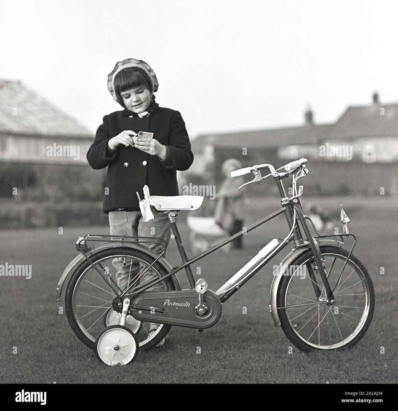 1960s, historical, a young girl standing outside in a garden area with her Pavemaster bicycle with stablishers, England, UK. The bicycle was made by The Trusty Manufacturing Co at Edmonton, London, N18. Stock Photo