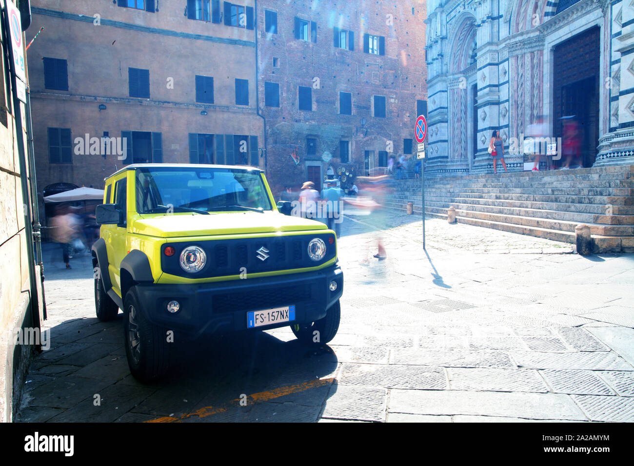 Sienna, Italy - A slow shutter motion shot of tourists, local people moving around a piazza in the city. The parked car a Jeep is still and in focus. Stock Photo