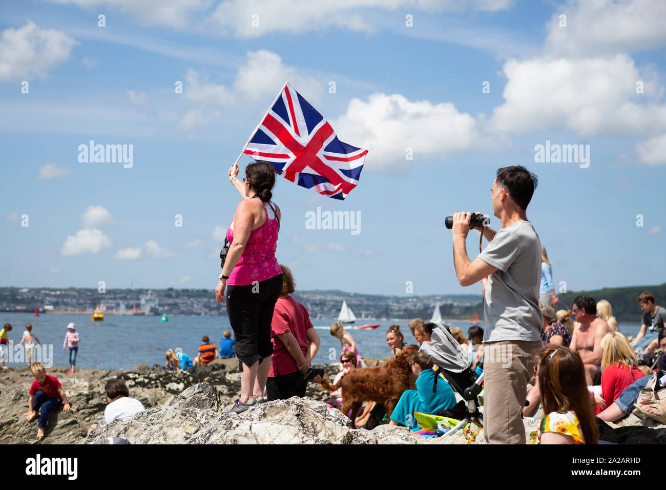 A woman holding the British Union Jack flag and a man with binoculars on the seaside in St. Mawes, Cornwall, Great Britain. Public gather on the beach watching the RNLI (Lifeboats charity) Castle to Castle Swim 2013.This event to fundraise money for the RNLI, lasts on the last day of the Truro and Penwith College Fal River Festival. Or just a symbolic picture to illustrate Brexit. Stock Photo