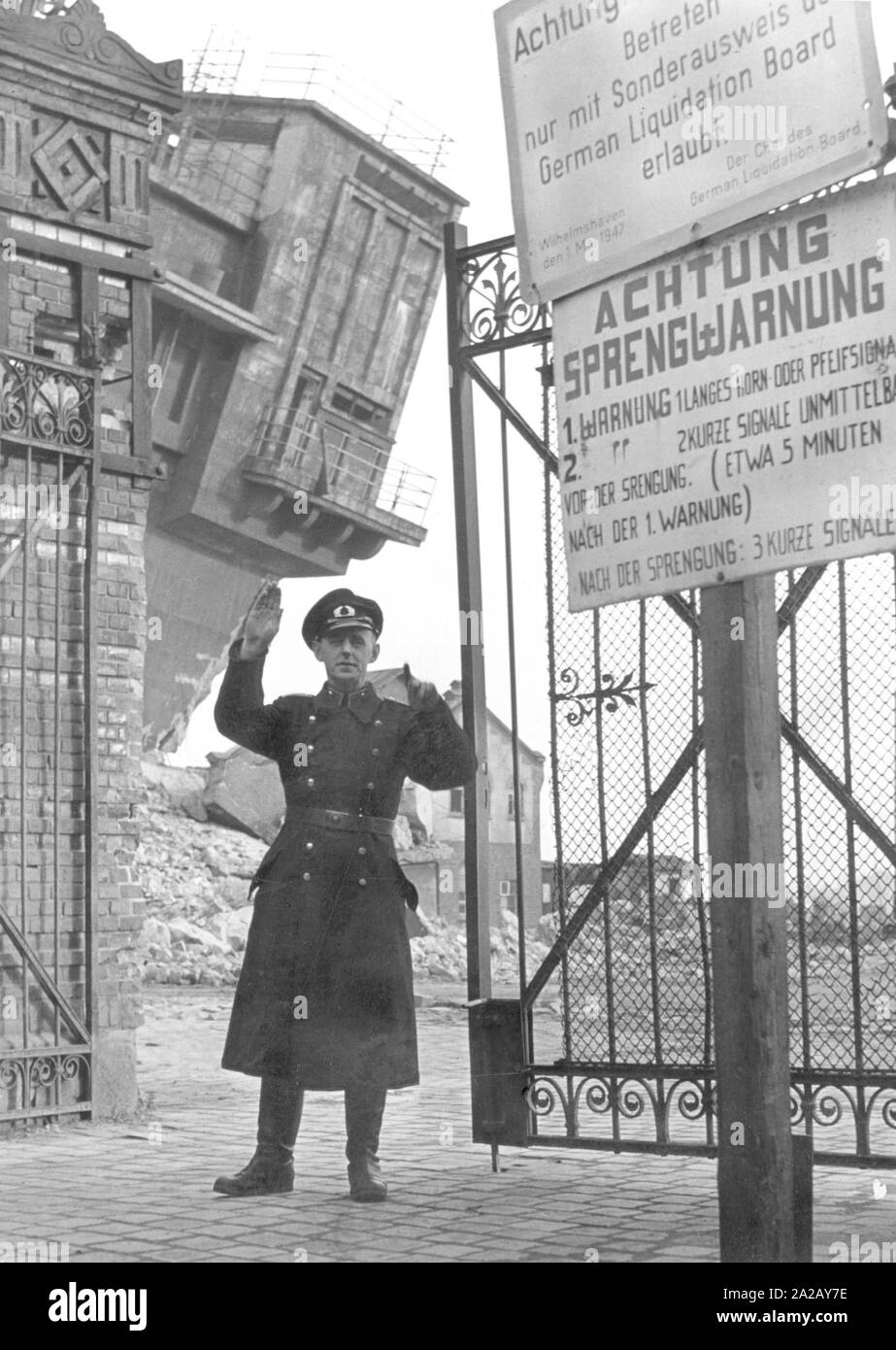 A guard at the gate to the port facilities in Wilhelmshaven. Right next to the gate there is a sign warning of blasting. The guard is a member of a plant security service or company police. Stock Photo