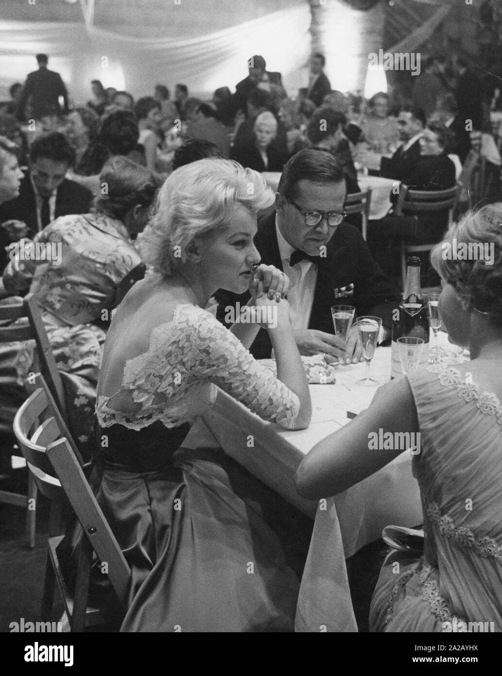 The radio host Karl Eduard Schnitzler and his wife, the actress Christine Laszar, sit at the table during the Defa-Filmball der Jugend (Defa Film Ball of Young People) in the company of women with a bottle of champagne. In the background, guests of the film ball. (undated picture) Stock Photo