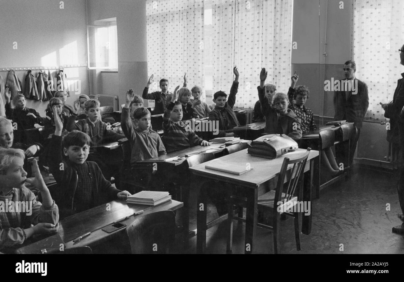 The picture shows a class in their classroom. The students react to a comment or question of the teacher by putting their hands up. Stock Photo