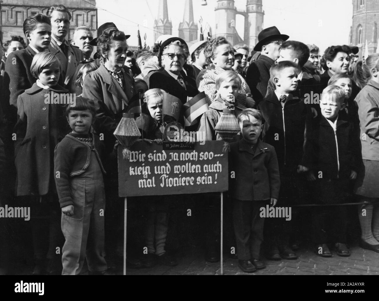 Citizens have gathered on the market place in Halle for the celebration of '10 years of GDR'. Kids hold a sign with the words: 'We are still soo small - and want to be pioneers once'. In the background: the Market Church. Stock Photo