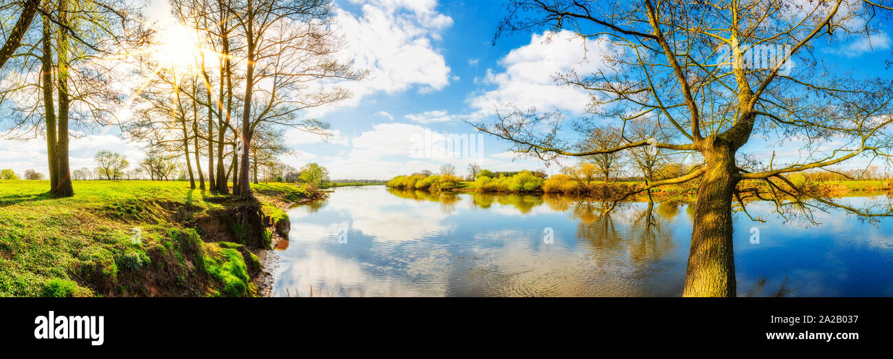 Panorama einer Landschaft im Frühling am Fluss mit Sonne, Wiesen und Bäumen Stock Photo