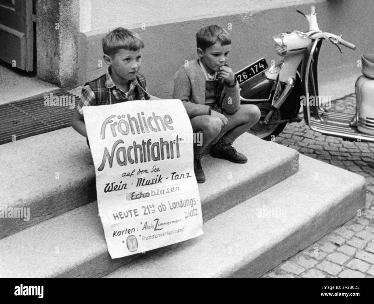 Two children with a poster of a tourist office promote a 'Cheerful night cruise on the lake'. Stock Photo