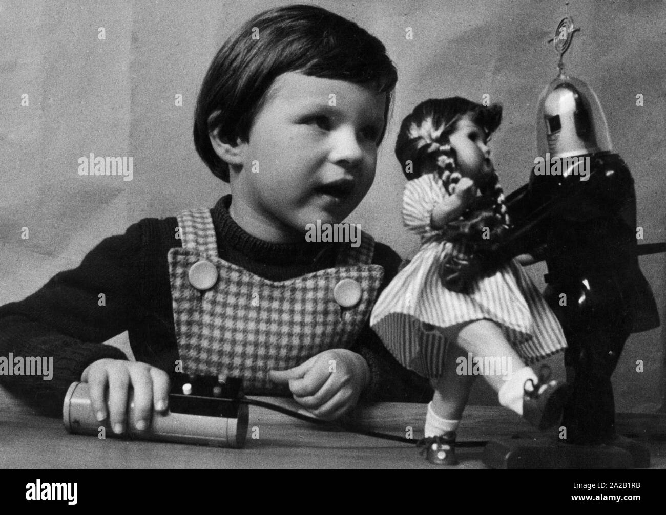 A girl plays with a doll and a toy robot. The novelty on the toy market is powered by two flashlight batteries and remotely controlled by four buttons. On command, he walks forward, bends, raises his arms, lowers them, takes them apart or together. He grabs and holds objects weighing up to fifty grams. Copyright: Max Scheler / SZ Photo. Stock Photo