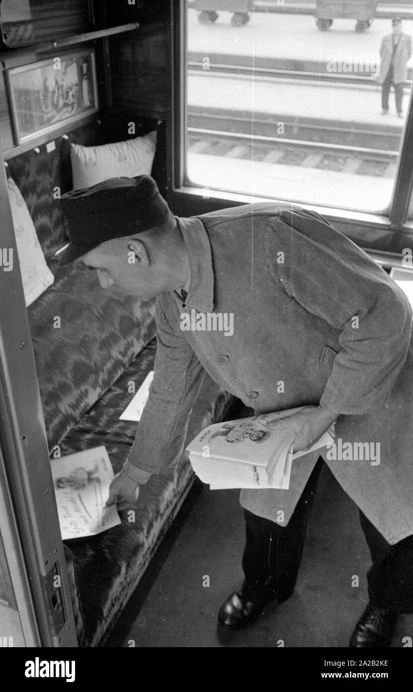 An employee of the Deutsche Bundesbahn (German Federal Railway) distributes advertisment leaflets for a competition in an empty compartment of a train. In cooperation with the 'Hoer zu!' ('Listen!'), one could win travel vouchers for a train journey at the Mecki contest. The train is standing on a track of Muenchen Hauptbahnhof. Stock Photo