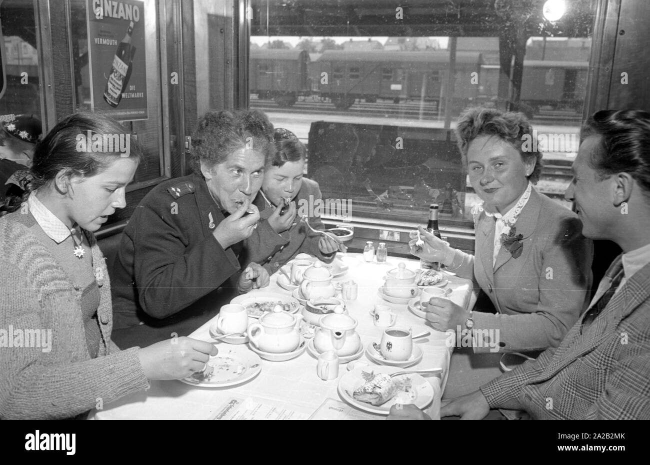 Photo of the interzonal train on the route Leipzig-Gutenfuerst-Hof-Munich. This train was known for its 'all-German' dining car, which was popular due to the 1: 1 exchange rate, especially among East German travelers. Photo of train passengers drinking coffee and eating cake in the dining car. The East German railway employee (left) with her two children sits at the table together with a woman from Munich and a student from the village. Stock Photo
