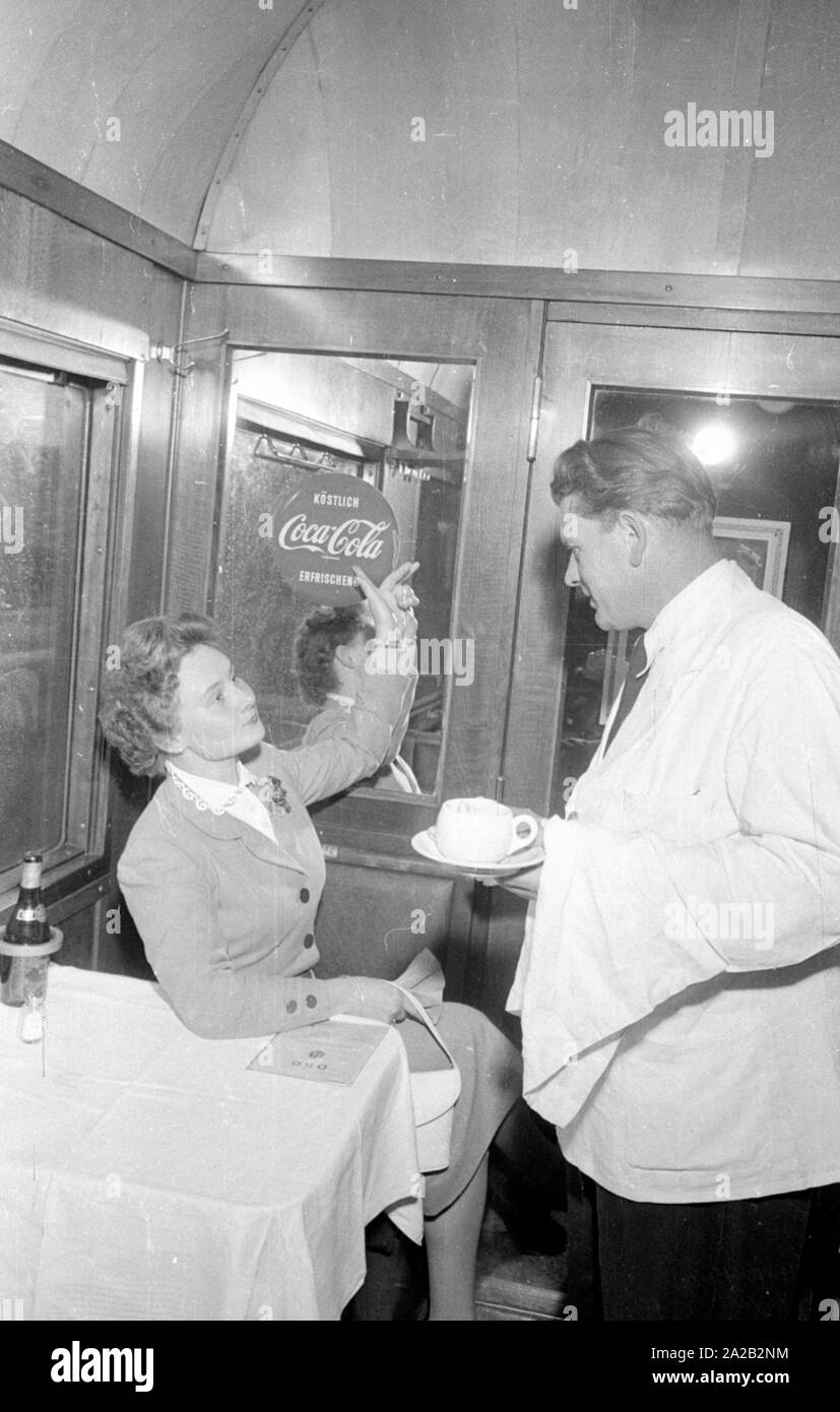 Photo of the interzonal train on the route Leipzig-Gutenfuerst-Hof-Munich. This train was known for its "all-German" dining car, which was popular due to the 1: 1 exchange rate, especially among East German travelers. Photo of a lady wanting to order Coca Cola from the waiter. However, since the administration of East Germany prohibited the sale of American products in this dining car, the drink was also unavailable. The billboard hangs there anyway. Stock Photo