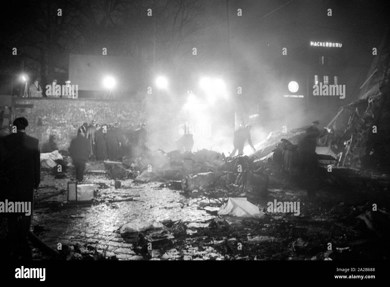 Shortly after the take off from the Munich-Riem Airport a US Air Force transport aircraft of the type Convair C-131-D Samaritan crashed in the area of Bayerstrasse / Martin-Greif Strasse on a tram. 52 people were killed. The picture shows the crash site illuminated with headlights, sightseers, relief forces and wreckage. In the background, the Hackerhaus. Stock Photo
