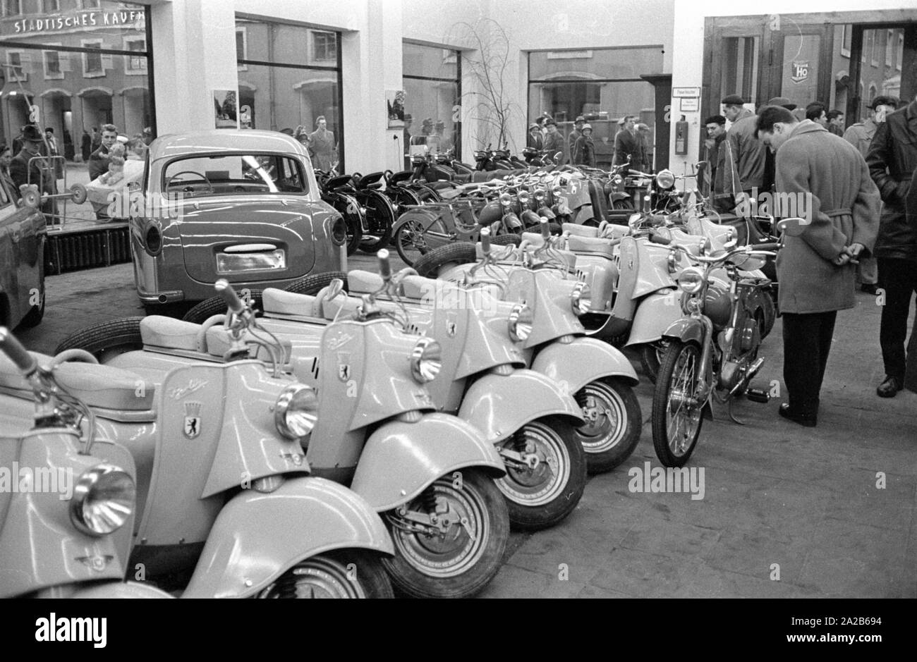 The city during the Spring Fair 1960. A man in front of a row of vehicles  produced in the GDR. Front row: IWL SR59 Berlin scooter (Berliner Roller),  back row: Simson SR