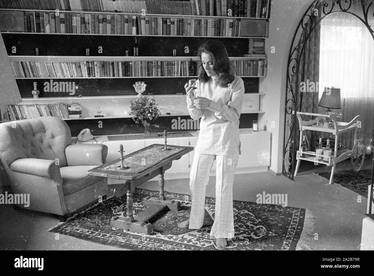 The German actress Karin Dor is photographed in her (?) living room. She holds a wine glass in her hand, to her right is a bar. Stock Photo