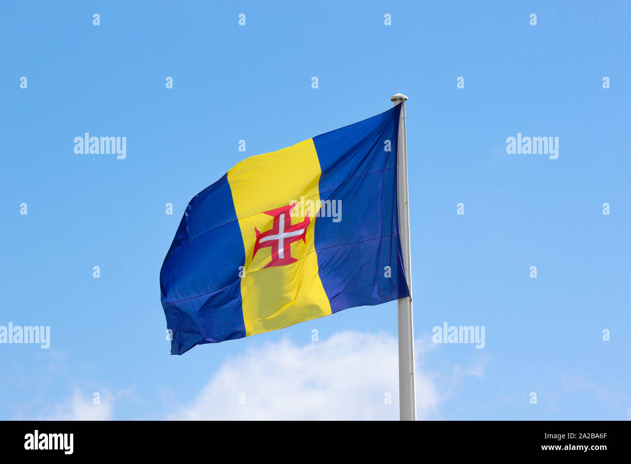 Waving flag of Madeira with blue sky in the background. It consists of a  blue-gold-blue vertical triband with a red-bordered white Cross of Christ  in the center. Portuguese island in Atlantic ocean