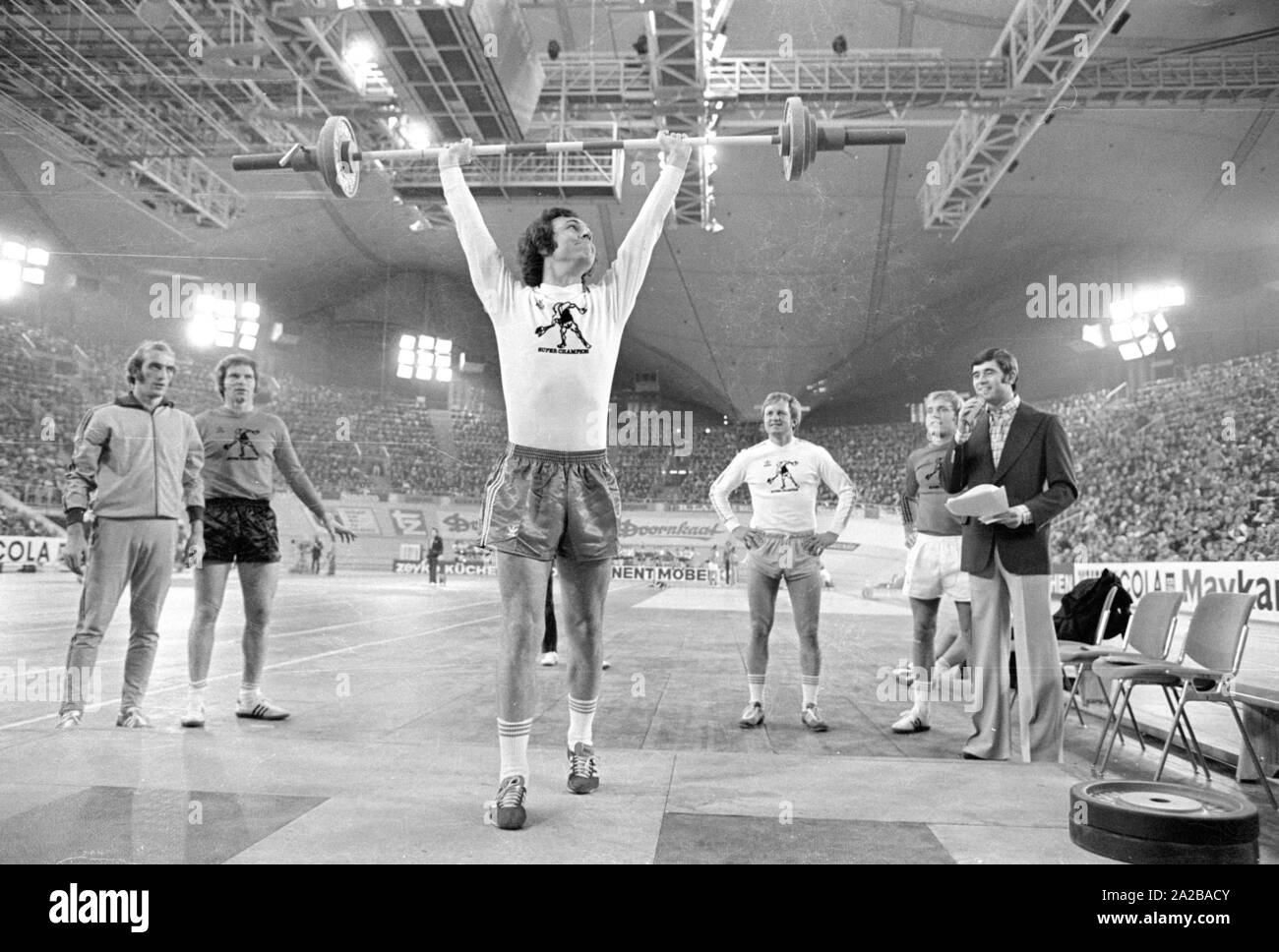 Footballer Franz Beckenbauer (center) dabbles in weightlifting at the Sportpressefest in the Munich Olympiahalle. Right in the picture, the athlete and moderator Erhard Keller. Stock Photo