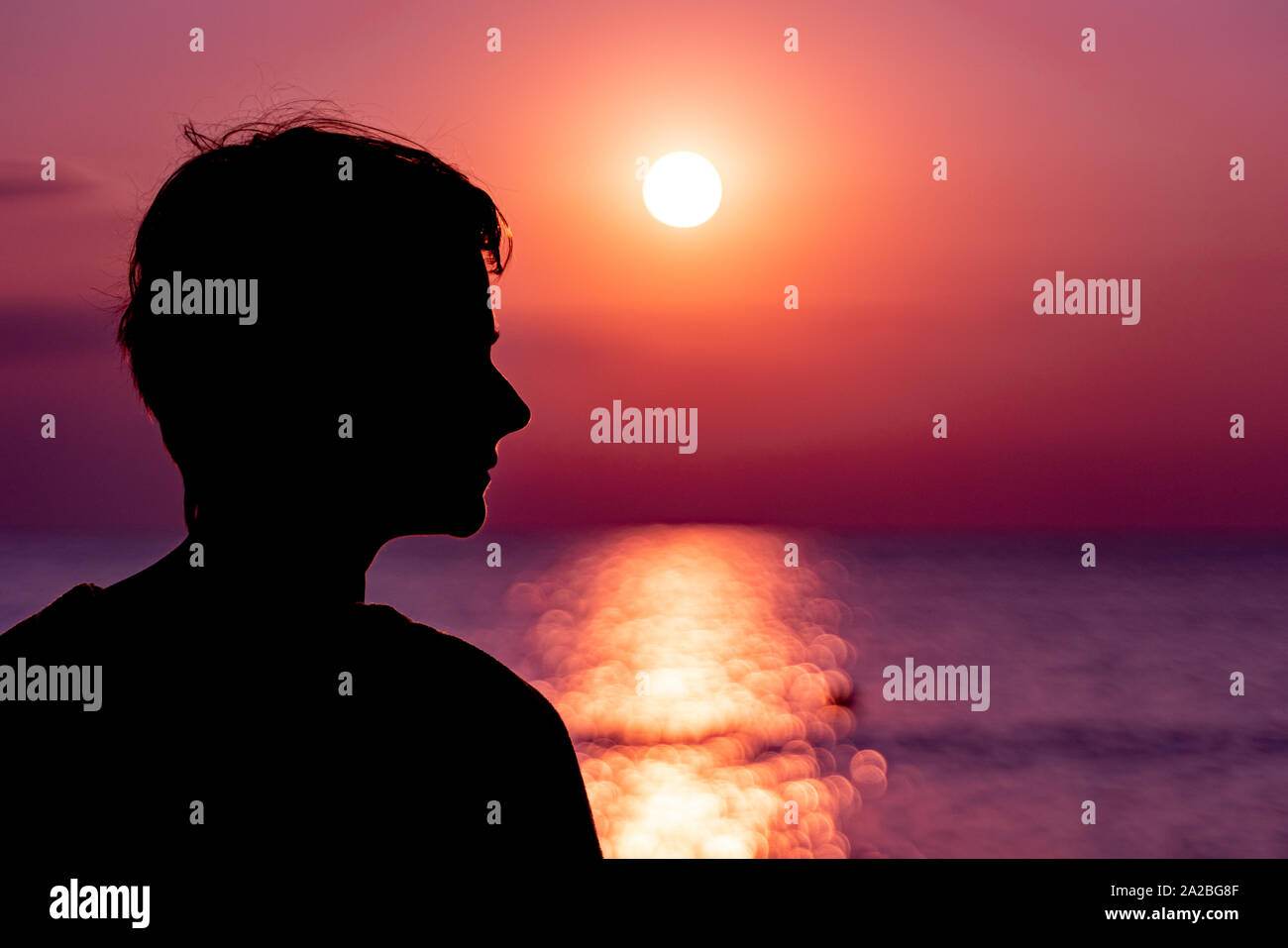 Girl in the shadows of the setting sun on the sea. Stock Photo