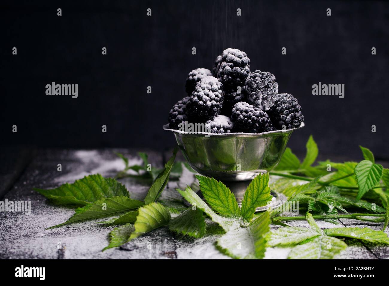 Blackberries Served With Sprinkled Powdered Sugar and Blackberry Leaves On Rustic Wooden Table. Stock Photo