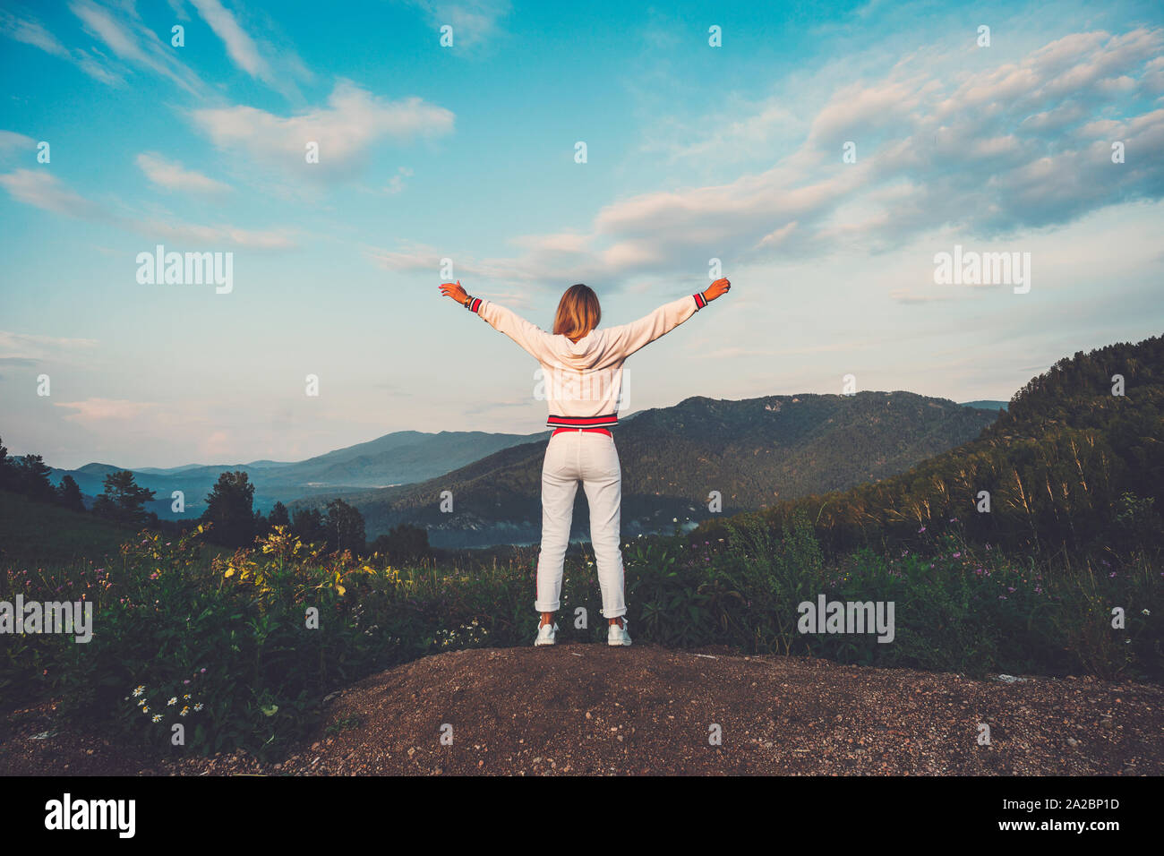 Happy celebrating winning success woman in white clothes standing elated with arms raised up above her head in celebration of having reached mountain Stock Photo